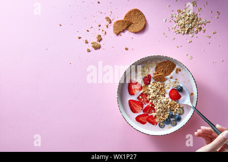 Donna di mani tenendo un cucchiaio, tazza di yogurt biologici smoothie con fragole, banana, mirtillo, fiocchi di avena e biscotti sul Foto Stock