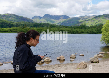 Una giovane donna ignorando il Lake District scenario di concentrarsi sul suo telefono cellulare, Elterwater, REGNO UNITO Foto Stock