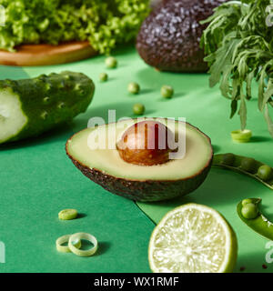 Organico fresca verdura verde - metà di avocado, calce, cetriolo, verde su una bicromia sfondo della carta. Foto Stock