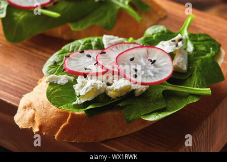 Luce panini sani con crostini di pane, formaggio morbido e fresco organici riuniti ravanelli, spinaci su una tavola di legno. Foto Stock