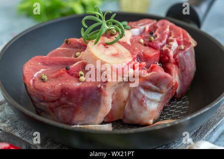 Pezzo di materie di stinco di manzo per osso buco e un rametto di rosmarino. Foto Stock