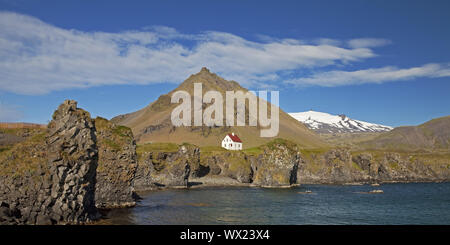 Casa sulla costa di basalto off Stapafell mountain e Snaefellsjoekull ghiacciaio, Arnarstapi, Islanda Foto Stock