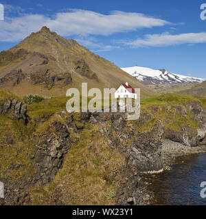 Casa sulla costa di basalto off Stapafell mountain e Snaefellsjoekull ghiacciaio, Arnarstapi, Islanda Foto Stock