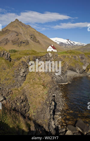 Casa sulla costa di basalto off Stapafell mountain e Snaefellsjoekull ghiacciaio, Arnarstapi, Islanda Foto Stock