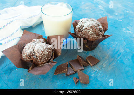 Due muffin al cioccolato, cioccolato nero e un bicchiere di latte su uno sfondo blu Foto Stock