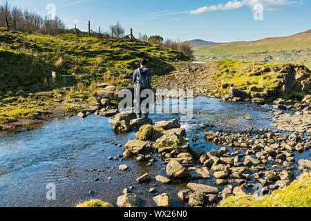 Un viandante utilizzando pietre miliari per attraversare il Lon un t-Stratha stream in Glen Uig, Trotternish, Isola di Skye, Scotland, Regno Unito Foto Stock