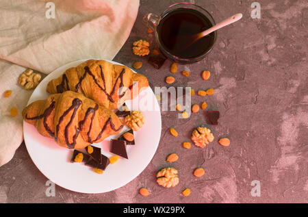 Due croissant al cioccolato di uvetta, noci e una tazza di caffè su sfondo grigio. Vista dall'alto. Concetto di colazione. Foto Stock