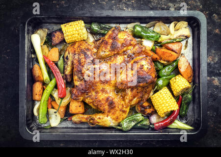 Spatchcocked barbecue pollo al mattone chili con mais e verdura come vista dall'alto su un vecchio foglio di metallo Foto Stock