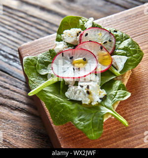 In casa la bruschetta con fettine di ravanello, foglie di spinaci e ricotta con semi di lino su una tavola di legno tagliato board. Foto Stock