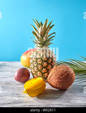 Frutti esotici e tropicali di foglie di palma sul pastello blu sullo sfondo - mango e ananas, carambole, noce di cocco, sul grigio di un tavolo di legno. Foto Stock