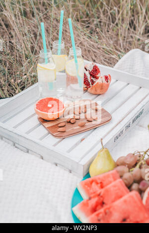 Set Picnic con succo di pompelmo, melograno, mandorle noci, angurie, uve e limonata in bottiglie di vetro bianco sul vassoio. Foto Stock