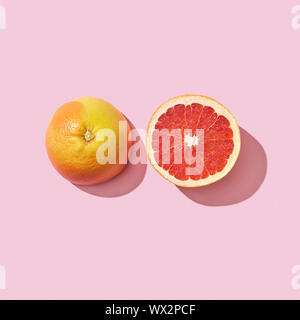 Due metà di un pompelmo maturi su uno sfondo rosa con la riflessione dell'ombra e spazio per il testo. Vitamina cibo sano. Parte superiore Foto Stock