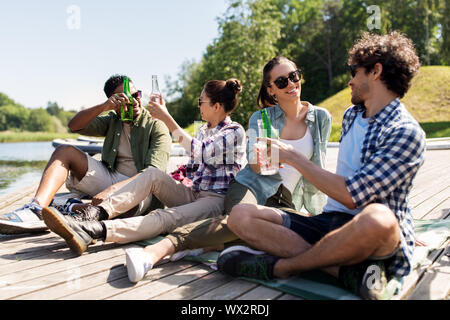 Gli amici a bere birra e sidro sul lago di pier Foto Stock