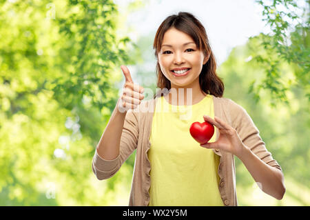 Felice donna asiatica con cuore rosso mostra pollice in alto Foto Stock