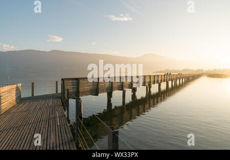 Lungo il molo di legno e la passeggiata sul lago di Zurigo vicino a rapperswill in golden luce della sera con silhou Foto Stock