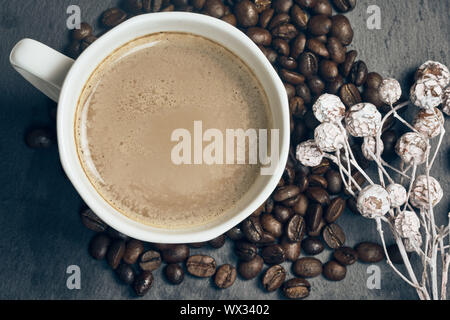 Vista superiore del caffè caldo in una tazza bianca con chicchi di caffè tostati e autunno decorazione su sfondo di ardesia Foto Stock