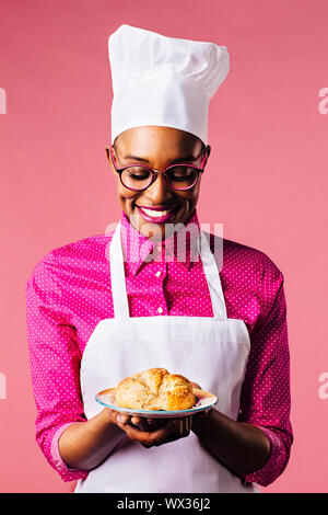 Ritratto di un sorridente giovane chef femmina tenendo una piastra con una fresca fatta croissant Foto Stock