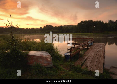 Estate tramonto su un fiume boscoso con barche invertito e un vecchio molo in legno Foto Stock