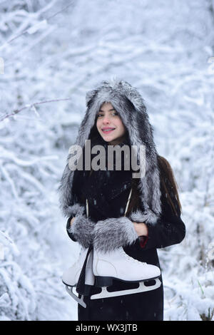 Ragazza sorriso con la coppia di figura pattini ad alberi nella neve. Donna con scarpe di pattinaggio in inverno abiti in boschi innevati. Sport, attività, salute. Skati ghiaccio Foto Stock