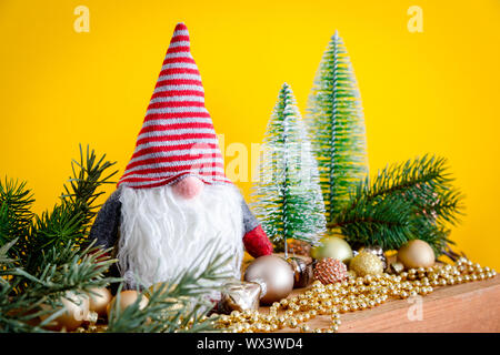 Decorazione di natale con un gnome su una scatola di legno e sfondo giallo Foto Stock