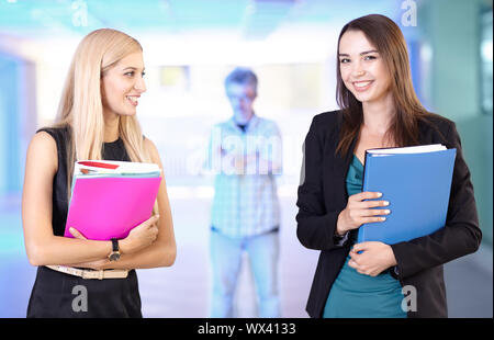 Due ragazze in ufficio con le cartelle con le carte in mano. Arrabbiato boss orologi da dietro. Foto Stock