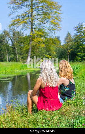 Due giovani donne caucasici sedersi insieme a waterside Foto Stock