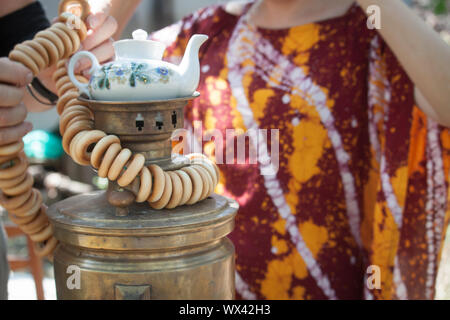 Mani femminili mettere bundle di bagel sulla parte superiore di un bronzo antico legno bruciando un samovar con una teiera su di esso, il fuoco selettivo Foto Stock