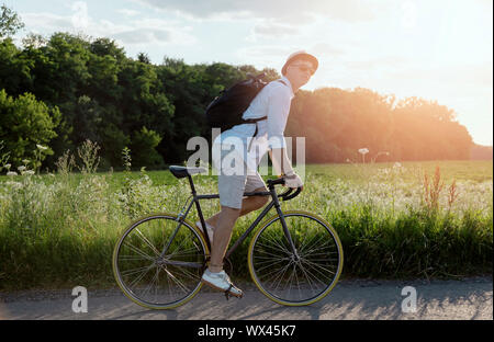 Giovane uomo in bianco indossando occhiali da sole godendo il suo rural viaggio in bicicletta Foto Stock