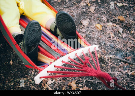Close up gambe femmina in stivali di tracking giacciono in un multi-colore striped amaca, il fuoco selettivo Foto Stock