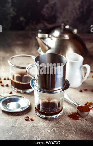 Caffè vietnamita in bicchieri di vetro e metallo tradizionale caffettiera phin. Il metodo tradizionale di lavorazione del caffè vietnamita Foto Stock