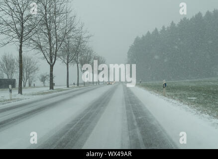 Tempesta di neve sulla strada di un paese e pericolose condizioni della strada in inverno con vetture di guida Foto Stock