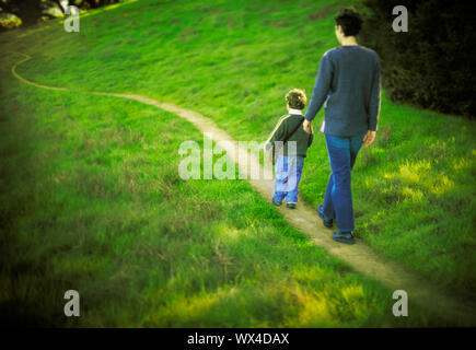 Un padre figlio duo passeggiata lungo un sentiero fra il verde. Foto Stock