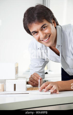 Ritratto di giovane maschio architetto sorridere mentre la creazione di un modello di casa Foto Stock