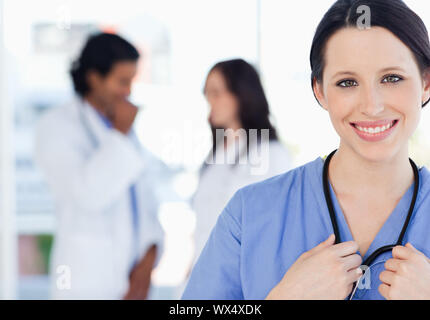 Giovane infermiere sorridente eretti accompagnati dal suo team che è in piedi dietro di lei Foto Stock