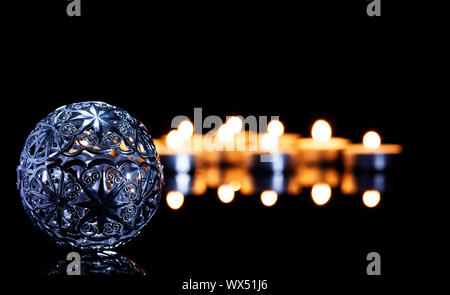 Metallo palla di Natale nella parte anteriore del tè candele su una black mirror Foto Stock