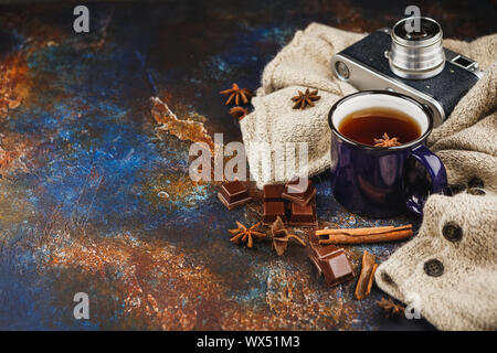 Smaltato blu tazza di tè, bastoncini di cannella, anice stelle, scuro pezzetti di cioccolato caldo maglione di lana e retrò fotocamera su uno sfondo scuro. Spazio per tex Foto Stock