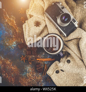 Smaltato blu tazza di tè, bastoncini di cannella, anice stelle, scuro pezzetti di cioccolato caldo maglione di lana e retrò fotocamera su uno sfondo scuro. Vista dall'alto. Foto Stock