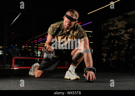 Un uomo muscoloso in un uniforme sportiva sorge sul pavimento Palestra facendo una pressa da banco con un kettlebell Foto Stock