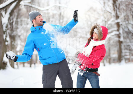 Carefree felice coppia giovane divertirsi insieme nella neve in inverno bosco tirare palle di neve a ogni altro durante la simulazione di una lotta Foto Stock