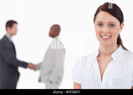 Commessa sorridente con mano i colleghi di scuotimento dietro di lei contro uno sfondo bianco Foto Stock