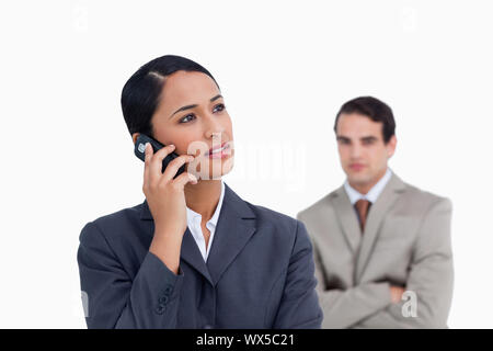 Commessa con il collega dietro di lei ascoltare attentamente per chiamante contro uno sfondo bianco Foto Stock