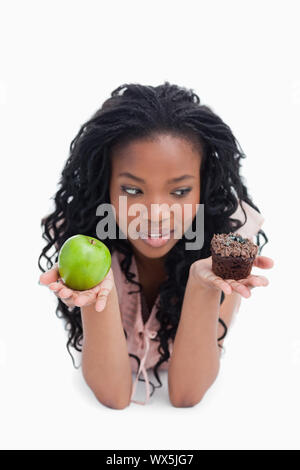 Una giovane donna è la scelta tra un Apple o un panino che essa detiene in su sulla sua palmi Foto Stock