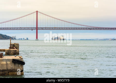 Vista verso il fiume Tago. Una nave cargo è ormeggiata vicino al XXV Aprile del Bridge Foto Stock