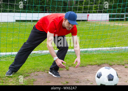 Giovane uomo con cappuccio come portiere la cattura di un pallone da calcio su un campo di calcio Foto Stock