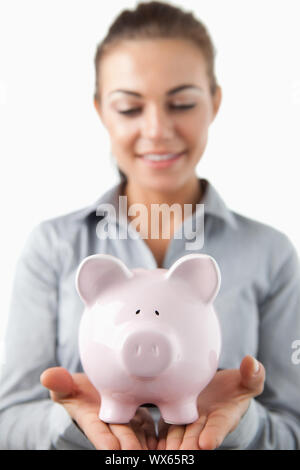 Close up di salvadanaio essendo tenuto dalla banca femmina assistant contro uno sfondo bianco Foto Stock