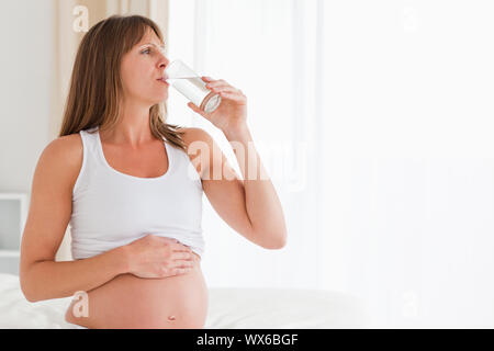 Bellissime le donne incinte di prendere una pillola mentre è seduto su un letto nel suo appartamento Foto Stock