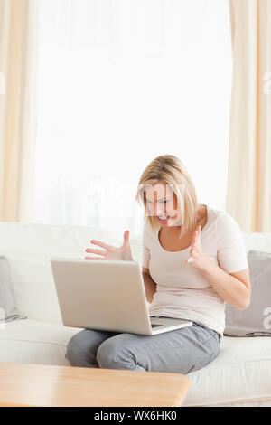 Il Portrait di sconvolgere un donna bionda con un computer portatile nel suo soggiorno Foto Stock