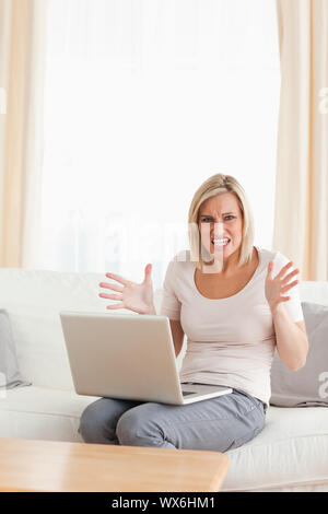 Il Portrait di un arrabbiato donna bionda con un computer portatile guardando la telecamera Foto Stock