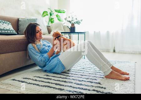 Giocando con il gatto di casa. Giovane donna seduta su un tappeto e abbracciando il pet. Foto Stock