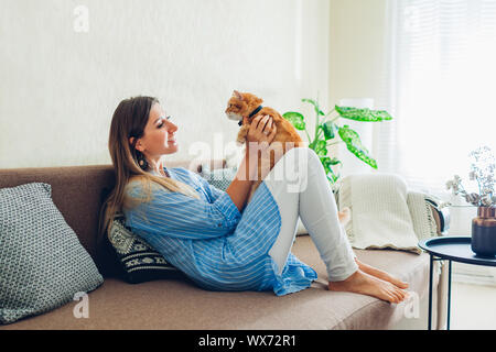 Giocando con il gatto di casa. Giovane donna seduta sul lettino e abbracciando il pet. Foto Stock